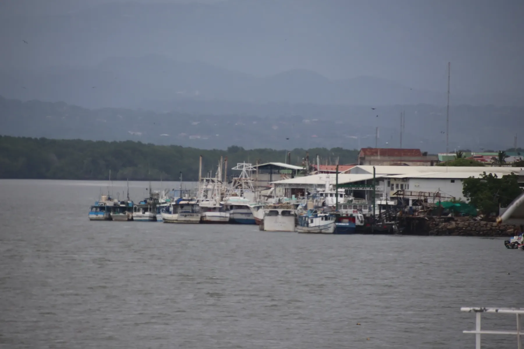 Fishing boats moored along a waterfront under hazy hills on the Costa Rica coast